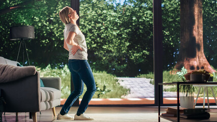 Young Adult Female Standing Up from a Couch at Home and Experiencing Back Pain in a Result of Spine Trauma. Massaging and Stretching the Back to Ease the Discomfort and Injury.