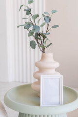 Portrait white picture frame mockup on table. Modern ceramic vase. Scandinavian interior. 