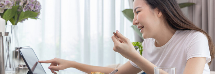 Asian woman eating fresh salad and using tablet at her home dining table, Vegetable salads are rich in vitamins and minerals, Fat-low-calorie and high-fiber diets, Healthy food, Appetizer.