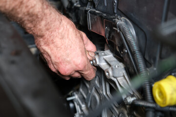 Fototapeta na wymiar Auto mechanic hands screws the engine mount after replace the timing belt. Mechanics workshop.