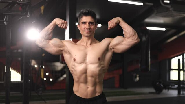 attractive shirtless mature male bodybuilder with perfect torso posing muscular body in gym
