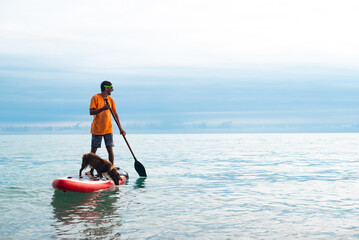 a guy on a sup board with a paddle with a dog stands on the sea in summer