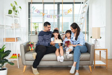 Asian family celebrating birthday together at home.Asian girl blow out candles on cake on table in happy birthday party and colors decorative items .