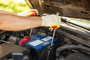 Battery replacement and repair. A car mechanic removes a car battery from under the hood of a car for replacement or charging