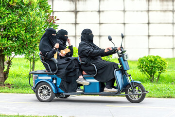 muslim women in in traditional wear burqas ride by electric bike scooter © welcomeinside