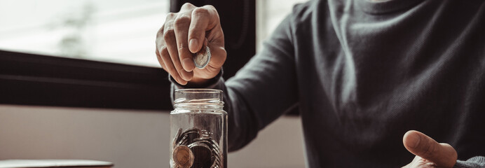 Man puts a coin dollar in a jar, Saving money for future growth and knowing how to manage your...