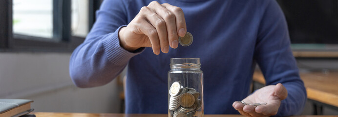 Man puts a coin dollar in a jar, Saving money for future growth and knowing how to manage your spending wisely, Saving money for business growth or long-term profitability.