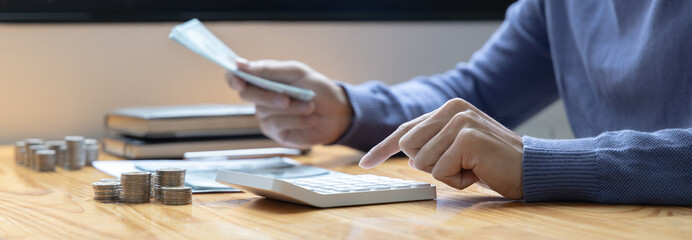 Man is pressing a calculator to calculate the amount he has accumulated over the year, Hand holding dollar bill, Saving money for the future, business investment, Finance and Accounting.
