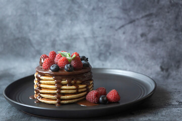 Pancakes with raspberries, blueberries and chocolate sauce on a wooden plate.