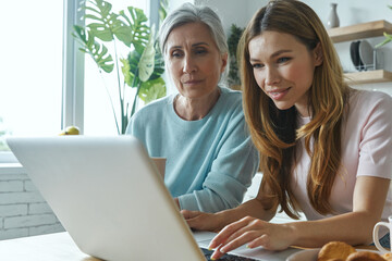 Senior woman and her adult daughter using laptop while spending time at home together