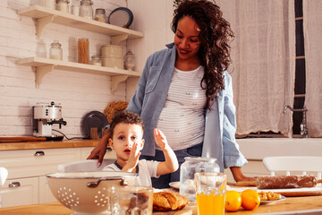 young pretty african american mother with little cute son on kitchen in morning preparing...