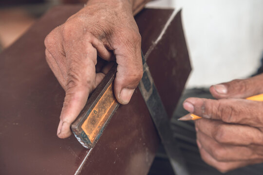 Drawing a straight line with a pencil and l-square on a piece of sheet metal. Marking guidelines for cutting. Hands of a grizzled veteran carpenter.