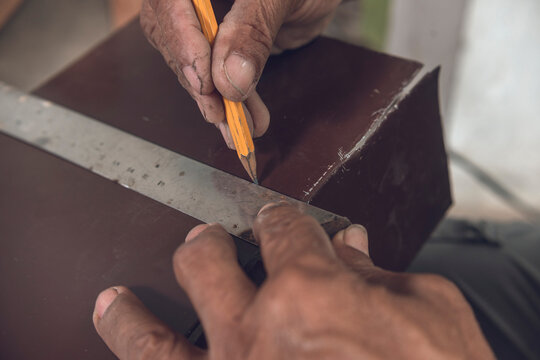 Drawing a straight line with a pencil and l-square on a piece of sheet metal. Marking guidelines for cutting. Hands of a grizzled veteran carpenter.