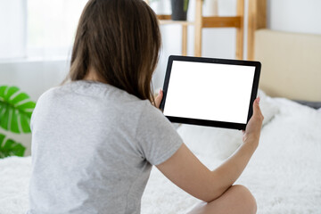 Video conference. Casual woman. Computer mockup. Unrecognizable lady looking tablet computer with blank screen sitting bed in light room interior.