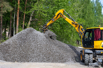  excavator takes a bucket of crushed stone from a large pile of rubble