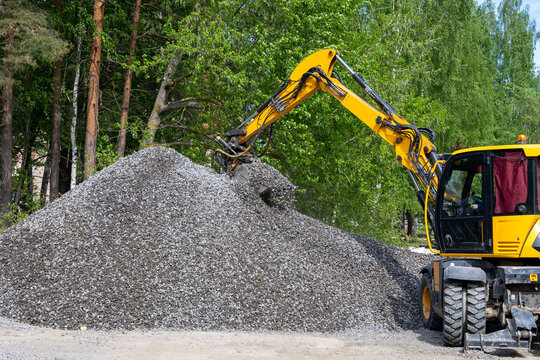  excavator takes a bucket of crushed stone from a large pile of rubble