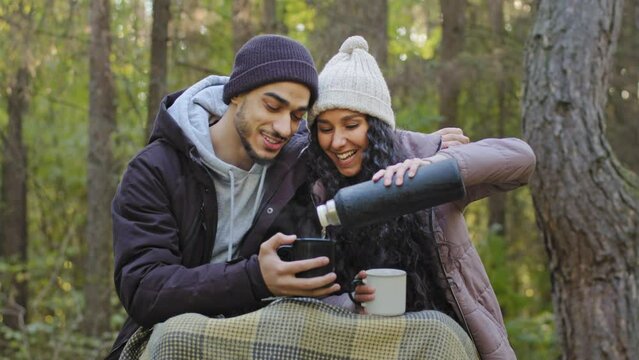 Young happy couple of tourists in love sit hugging in nature drinking hot tea from thermos to restore strength hikers relaxing outdoors warmed up with warm delicious drink romantic date in autumn park