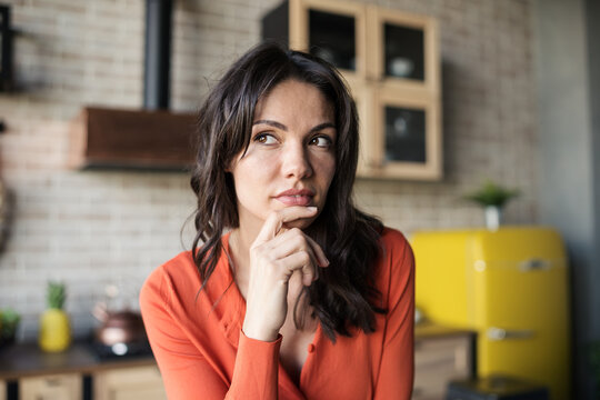 Portrait of beautiful brunette woman thinking or creating idea with her hand on chin in kitchen at home