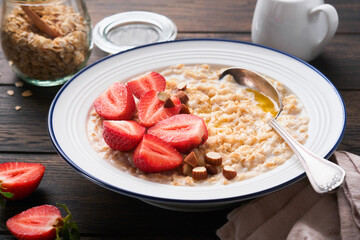 Oatmeal. Bowl of oatmeal porridge with strawberry, almond and milk on old wooden dark table background. Top view in flat lay style. Natural ingredients. Hot and healthy breakfast and diet food.