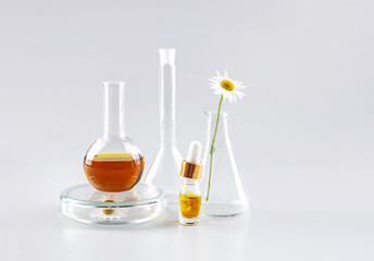 bottle with a pipette, laboratory flasks with a solution and a chamomile flower on a gray background. the concept of natural cosmetics and herbal medicine