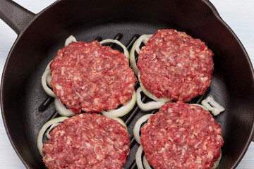 Raw burgers with onions in a frying pan.