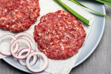 Raw beef burgers with onions on a grey plate.