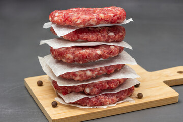 Raw beef burgers are stacked on board. Close up.