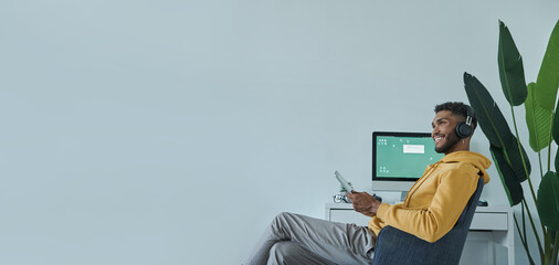 Dreamful African man holding digital tablet and smiling while sitting at his working place