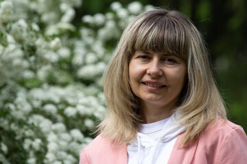 Fototapeta premium Woman smiling against the background of white flowers, with bangs, highlighting hair, without retouching, original frame