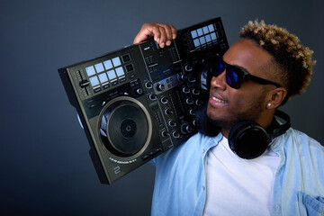 Cool guy with dark glasses on shoulder holds DJ console and carries club. Dark skinned DJ in...