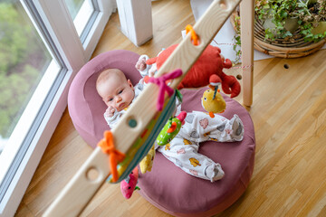 A newborn baby lies in a cocoon under hanging toys rattles