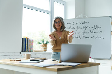 Happy senior woman gesturing while standing near the whiteboard at classroom