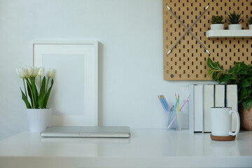 Front view of creative hipster desktop with laptop, stationery and photo frame with wall holder.
