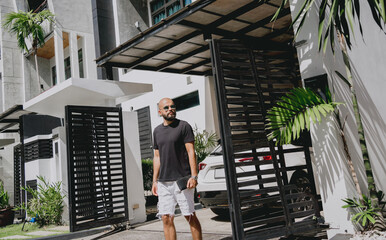 Young businessman walking out of his modern home with garage and car