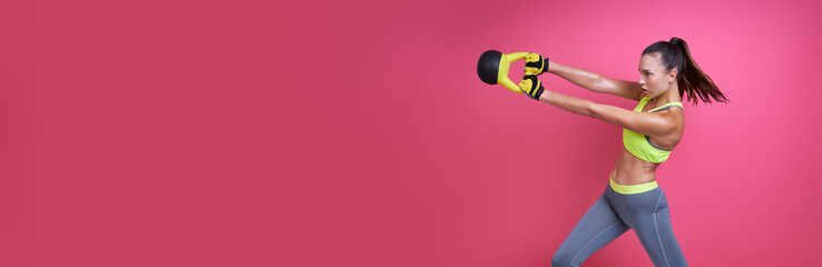 Confident young woman exercising with kettlebell against pink background