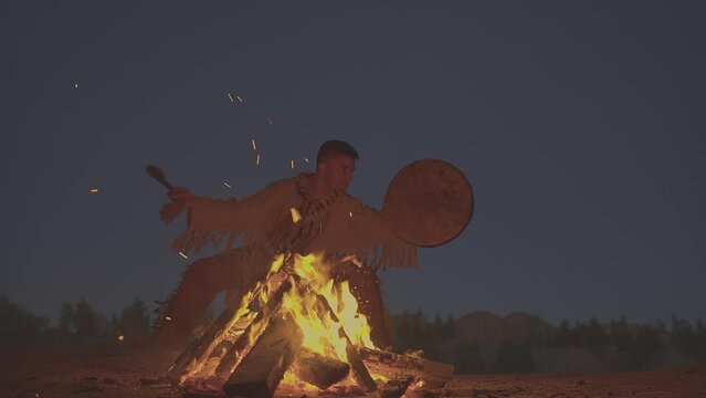 A shaman with a drum jumps in around the fire in clothes for the ceremony.