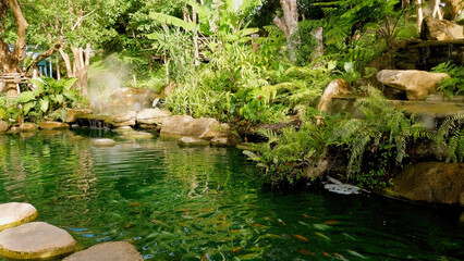 Naklejka na ściany i meble Beautiful pond with colorful koi fish among tropical green trees and greenery. Summer or spring nature landscape. Outdoor recreation, relaxation and calmness concept.