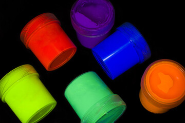 Fluorescent paint jars (red, yellow, orange, green, blue and purple) on a black background.