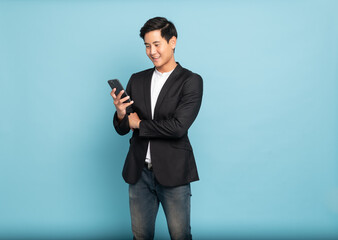 Young asian man in suit and jeans using smartphone for smart casual business concept isolated on blue background