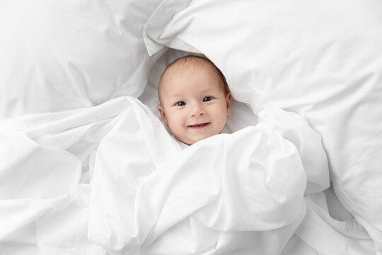 Happy newborn baby peeking from white sheet