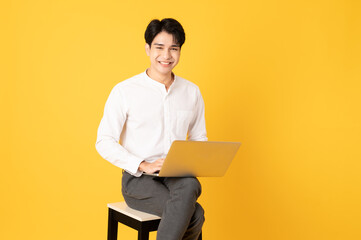 Smile happy asian man using laptop isolated on yellow background