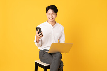 Smile happy asian man using laptop and smartphone isolated on yellow background