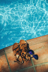 Sunglasses and women's sandals on the side of pool with clear turquoise water