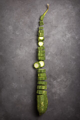 fresh angled luffa cut into slices on a black textured background, also known as ridged gourd or chinese okra, healthy vegetable taken from above with space for text