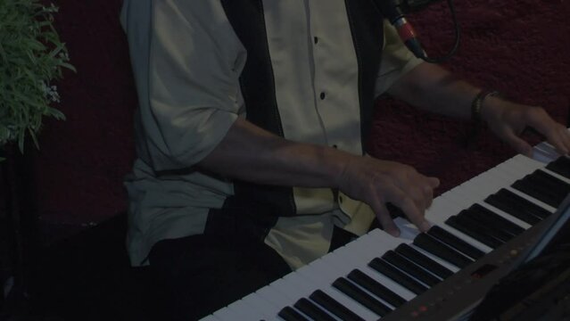 Piano player working the keys in a restaurant. Cinematic mode closeup of hands on the keyboard.