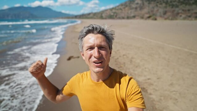 close up selfie portrait of happy middle aged greyhead man at sea coast enjoys sunny day on beautiful sandy beach Iztuzu in Turkey. inspired enjoyed man makes video call and talks about his place