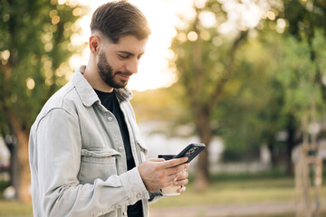 Handsome caucasian armenian young bearded man using phone stand on street at sunset. Mobile technology. Businessman cell modern fashion. Portrait. Outdoor