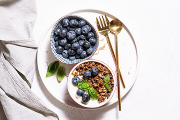 Homemade granola with yogurt and blueberries on the marble tray on white stone background top view. Healthy tasty breakfast concept.