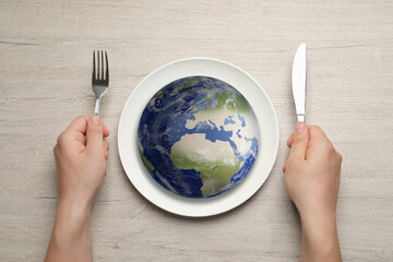 Global food crisis concept. Man with cutlery and globe of Earth in plate at wooden table, top view