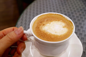 Hand holding a cup of cappuccino coffee with heart shaped latte art